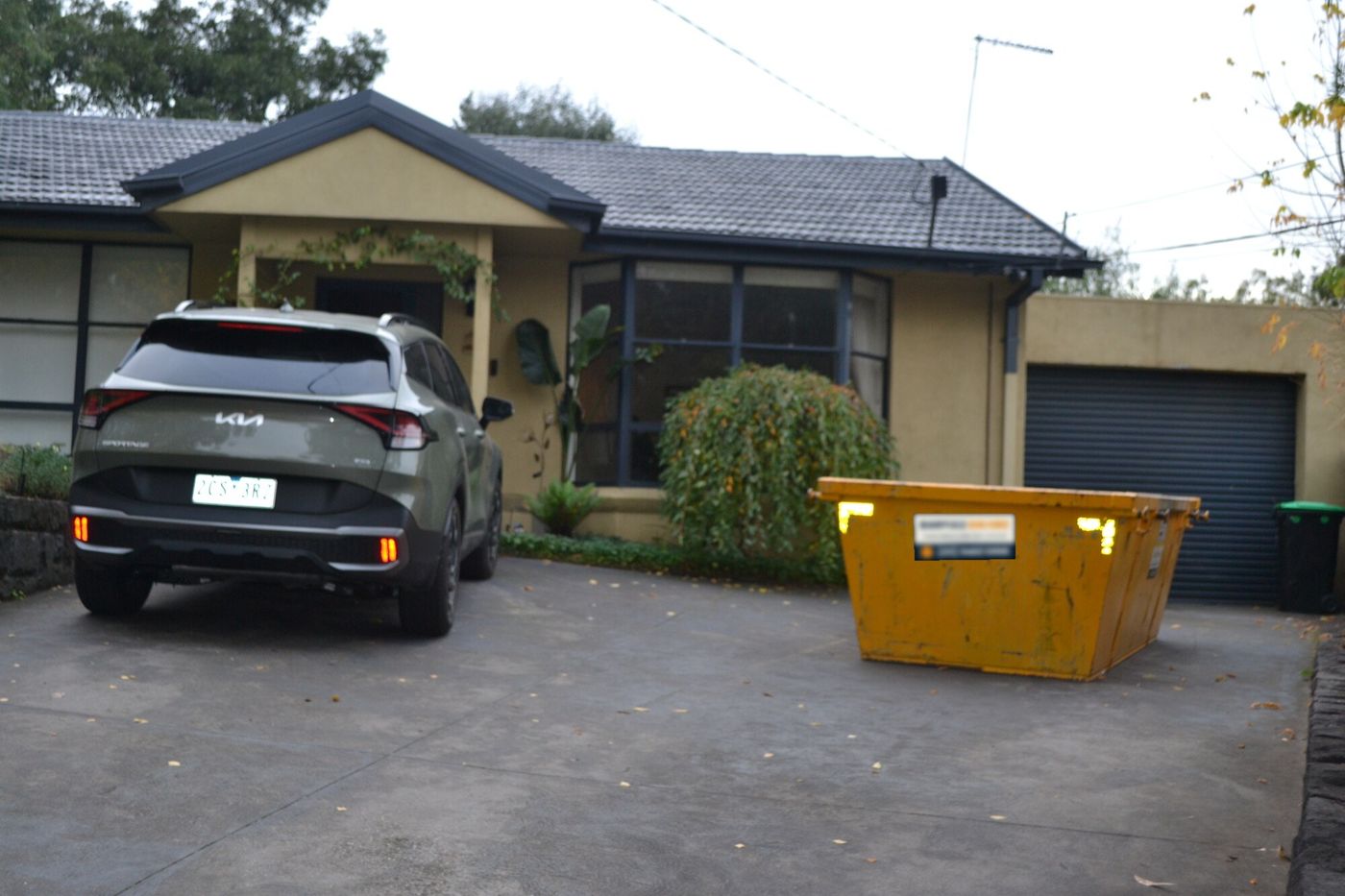 Skip bin on a residential driveway beside a car